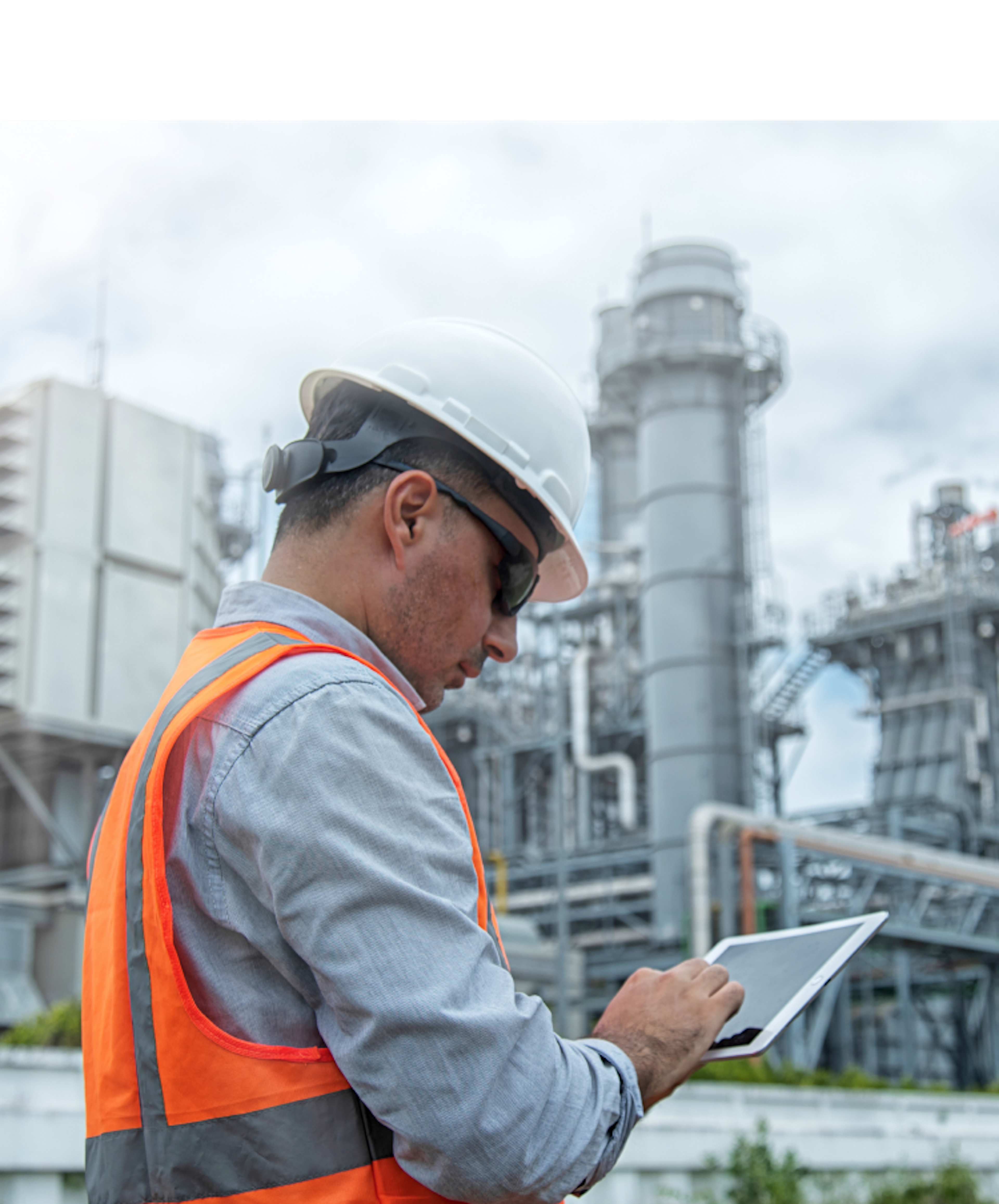 A person in a hard hat and vest facing industrial structures. The sky is partly cloudy, and their face is pixelated.