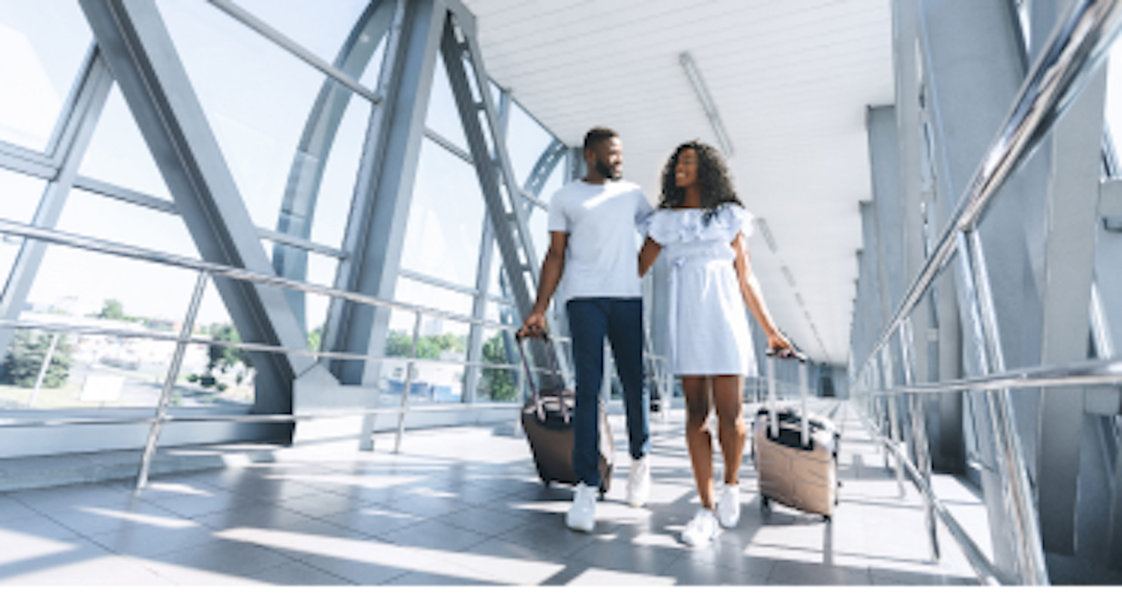 A couple walking on airport with their briefcases and smiling.