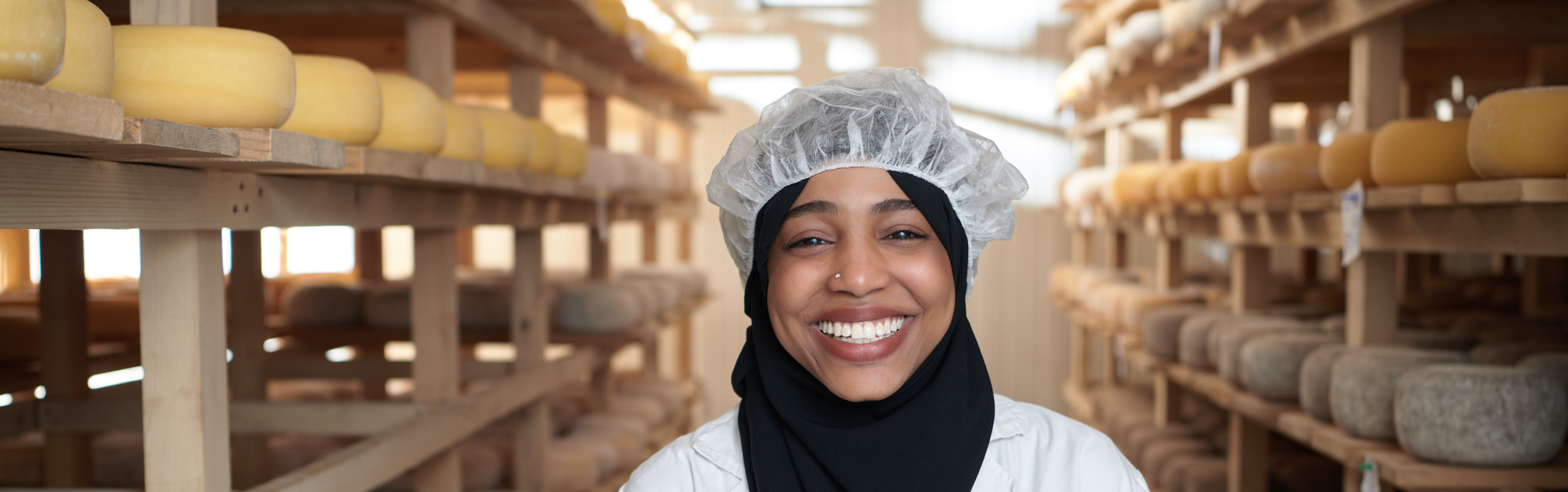 A person standing in a cheese aging room with shelves of cheese wheels