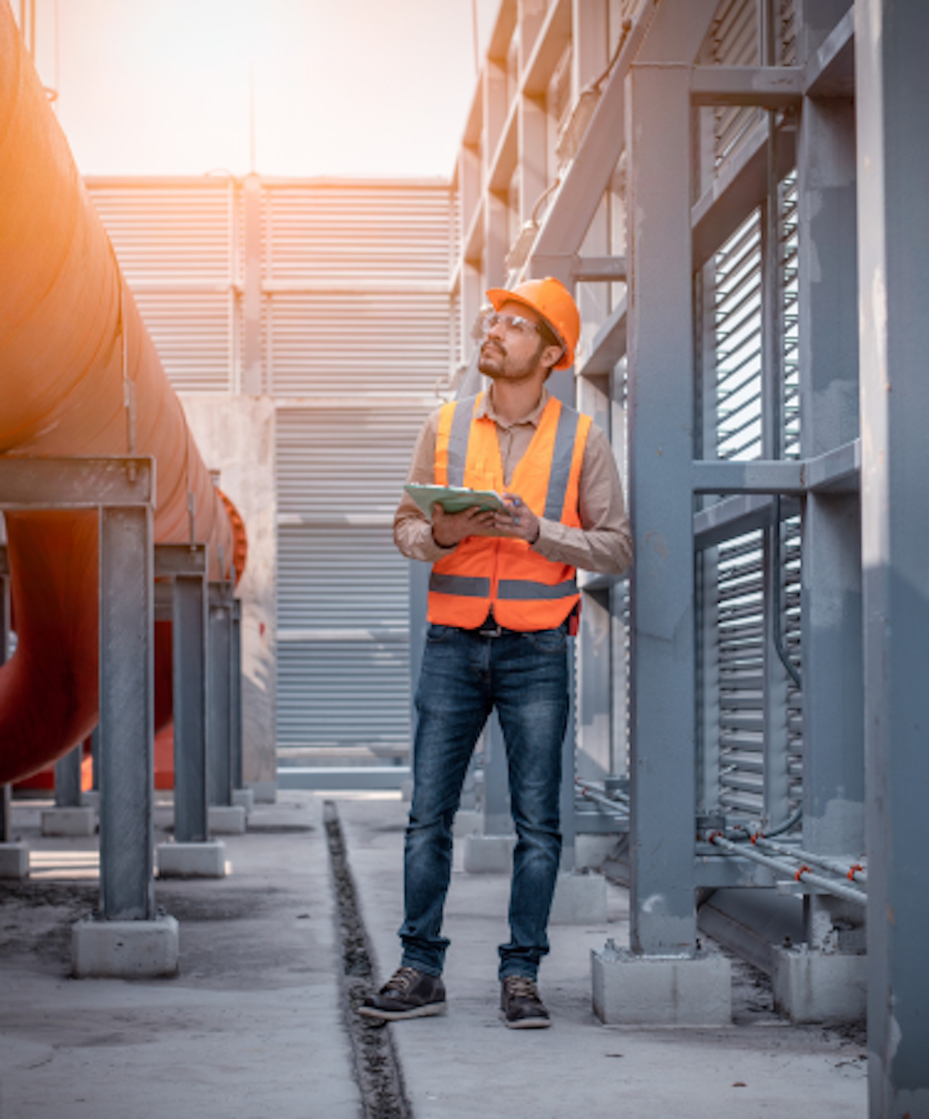 A construction worker wearing a hard hat, safety vest, and gloves is holding a tablet while standing on a metal staircase at a construction site.